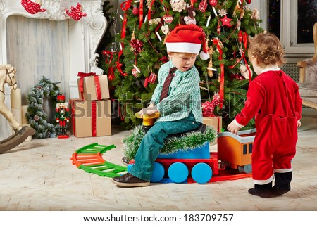 Little boy in Santa cap rides toy plastic steam engine at room decorated to Christmas celebration