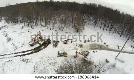 Aerial view to excavators on snow-covered ground reduced pond near the forest
