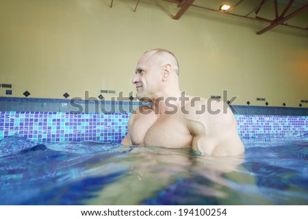 Wet bodybuilder looks away in pure water of swimming pool of gym hall