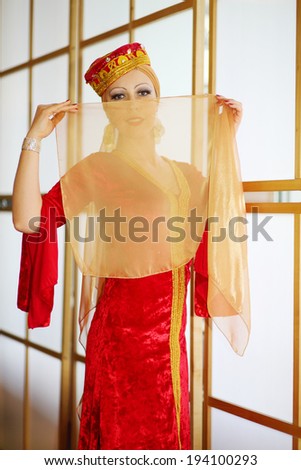 Young woman in red Andalusian costume hides face behind shawl