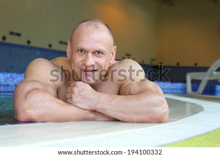 Happy bodybuilder relies on curb of swimming pool of gym hall