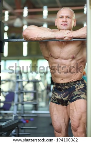 Handsome serious bodybuilder in shorts based on barbell in gym hall