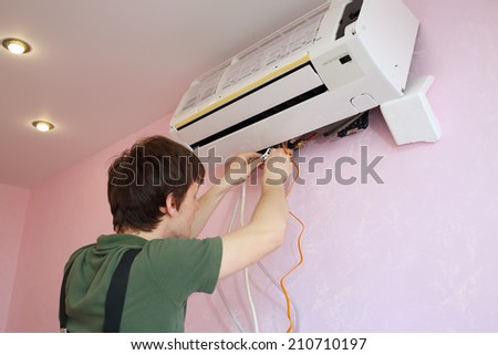 Young worker connects the wires to the new air conditioner in the living room