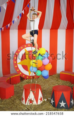 Little boy rises top rope ladder in striped circus tent
