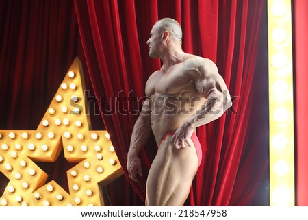 Strong man with big muscles standing on red stage with big lights star