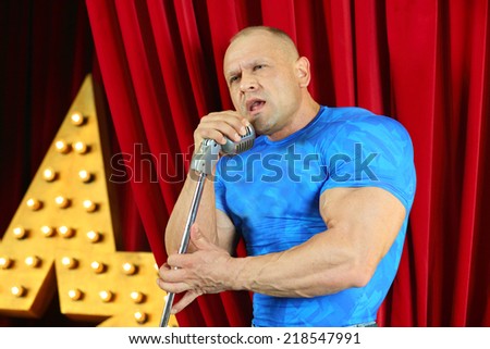 Handsome man in blue T-shirt standing with microphone on red stage and singing song