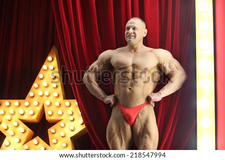 Strong man with big muscles shows his physique on red stage with big lights star