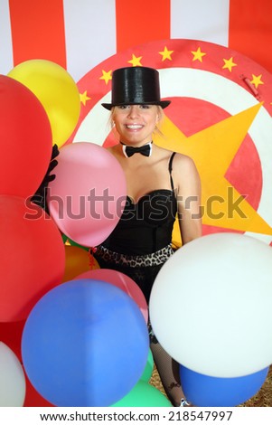 Happy circus performer in black hat with colored balloons in striped circus tent