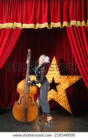 Beautiful woman in pop dress playing with contrabass on stage at music hall