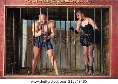 Strong man and beautiful woman in cage for animals
