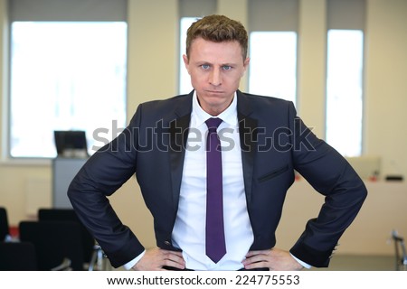 Portrait of young angry businessman with hands on hips in the office