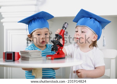 Small children in blue graduation hat adjust microscope on table