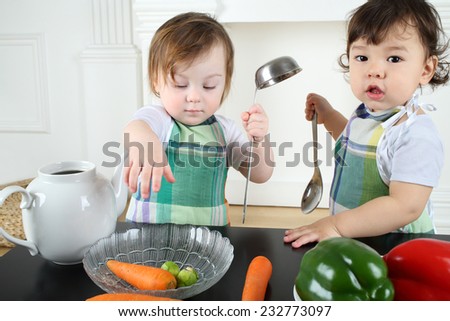 Two small children boy and girl in the kitchen apron play at a table with kitchenware and vegetables