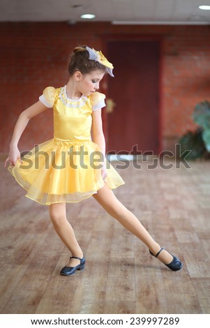 Beautiful girl in yellow satin dress dancing in hall with brick walls