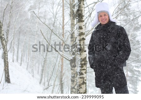 Portrait of smiling young man standing under snowfall in birch forest