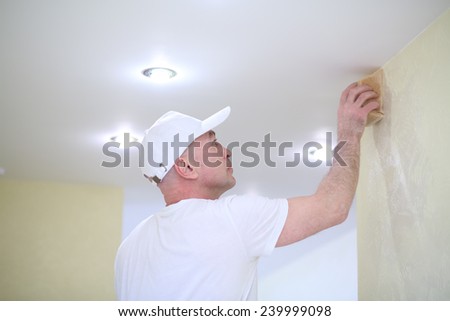 Finisher polishing the wall near the ceiling using a sanding sponge