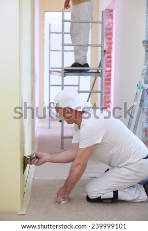 Finisher sitting on the floor inflicts the plaster on the wall using a pallet