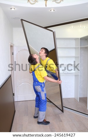 Young worker raises mirrored door on sliding wardrobe in room