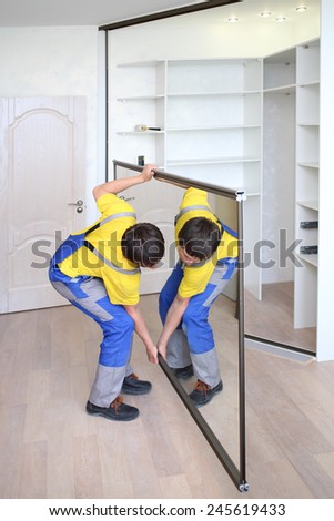 Young worker raises mirrored door on corner closet in room