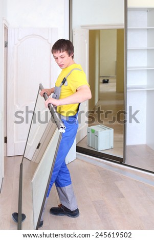 Young worker holding mirrored door on sliding wardrobe in room