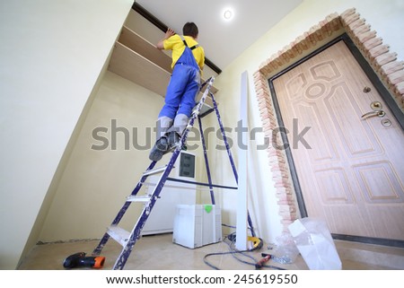Man standing on ladder fixes shelves to wall for closet in hallway, bottom view