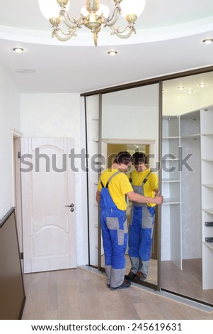 Young man fixing mirrored door on corner closet in room