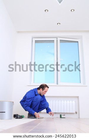 Worker in blue overalls laid wood floorboard in white room