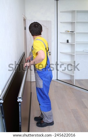 Man in workwear holding mirrored door on sliding wardrobe in room