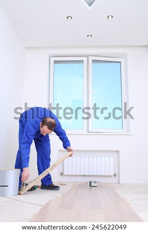Master applies glue to floorboard with spatula in white room