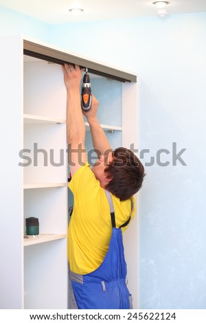 Man installing guide rails for sliding wardrobe in room with blue walls