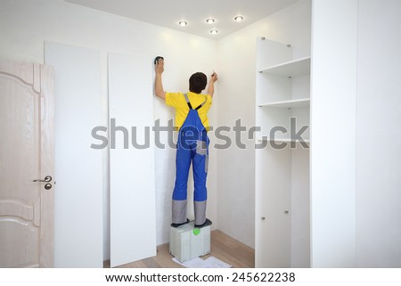 Man makes a mark on the wall to install a corner sliding wardrobe