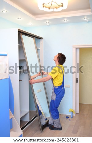 Young man setting door for sliding wardrobe in room with blue walls