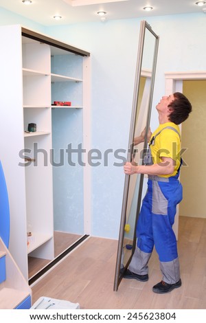 Worker setting door for sliding wardrobe in room with blue walls