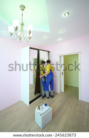 Young worker setting mirror door for sliding wardrobe in room with pink walls