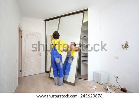 Worker setting mirrored doors on corner sliding wardrobe in room
