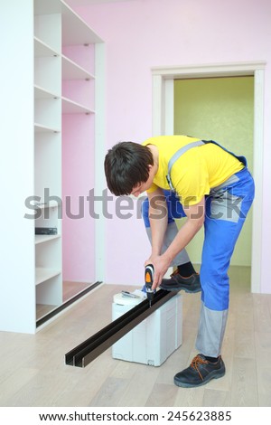 Worker installing guide rails for sliding wardrobe in room with pink walls