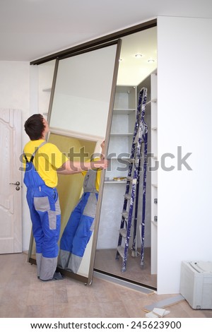 Man setting mirrored doors on corner sliding wardrobe in room