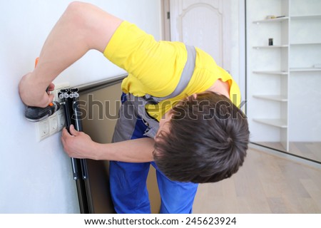Man using perforator sets of fastening on the door for sliding wardrobe