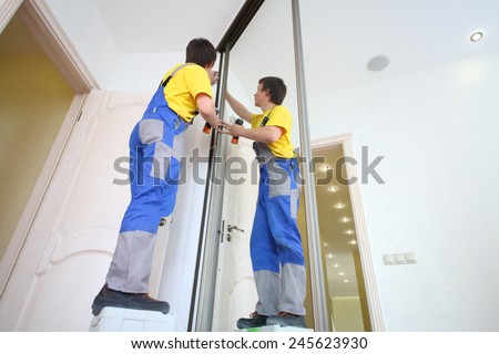 Young man in workwear fixing mirrored door on sliding wardrobe in room