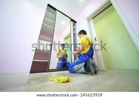 Young man sitting on the floor secures door sliding wardrobe in room with pink walls