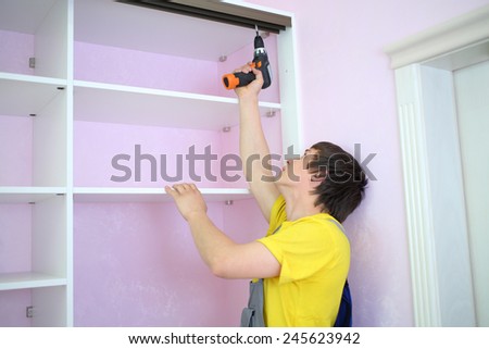 Man installing guide rails for sliding wardrobe in room with pink walls