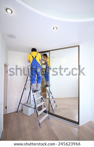 Young worker fixing mirrored door on sliding wardrobe in room