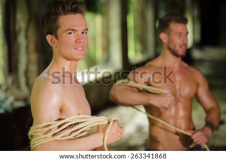 two young men stripped to waist is wrapped rope in his hands in abandoned building focus on left man