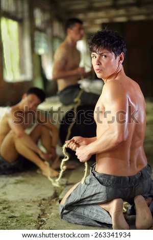 young man in ragged pants looks holds rope in his hands in abandoned building