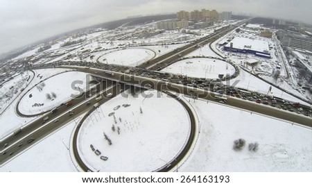 Cityscape with traffic on interchange of belt way at winter day during snowfall. Aerial view