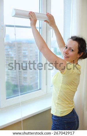 Happy woman wants to hang blinds on the window
