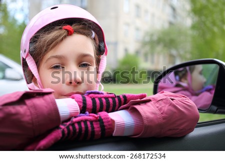 Girl in pink helmet leaning on the open window in the car