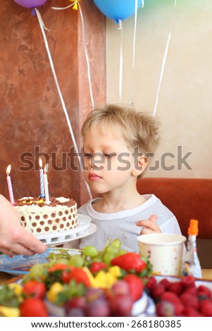The little boy looks at the birthday cake with candles in cafe