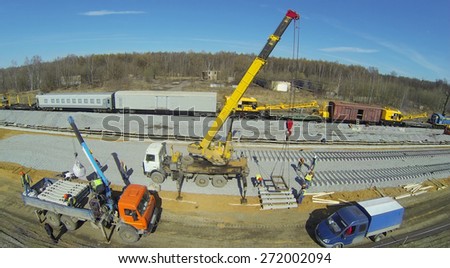 Building machines and crane with sleepers at construction of new railway next to wagons, aerial view