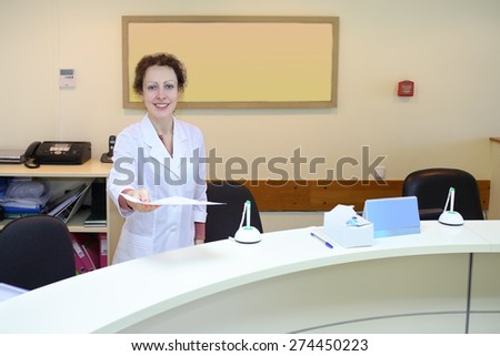 Medical worker in white coat holds out a sheet of paper at the reception